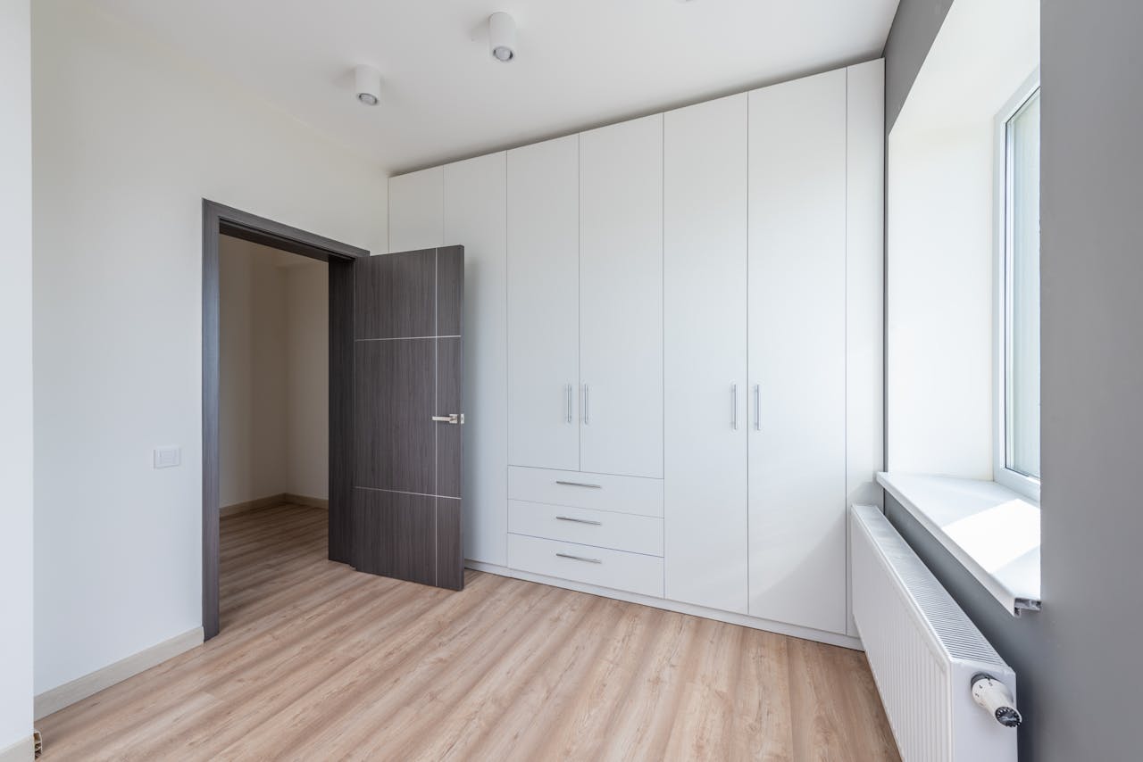 service-01 A bright, empty room featuring sleek white cabinets and wooden flooring, ideal for interior design concepts.